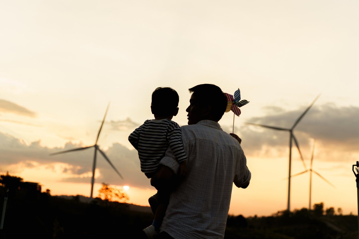 A parent and child in silhouette looking at field of wind turbines for renewable energy